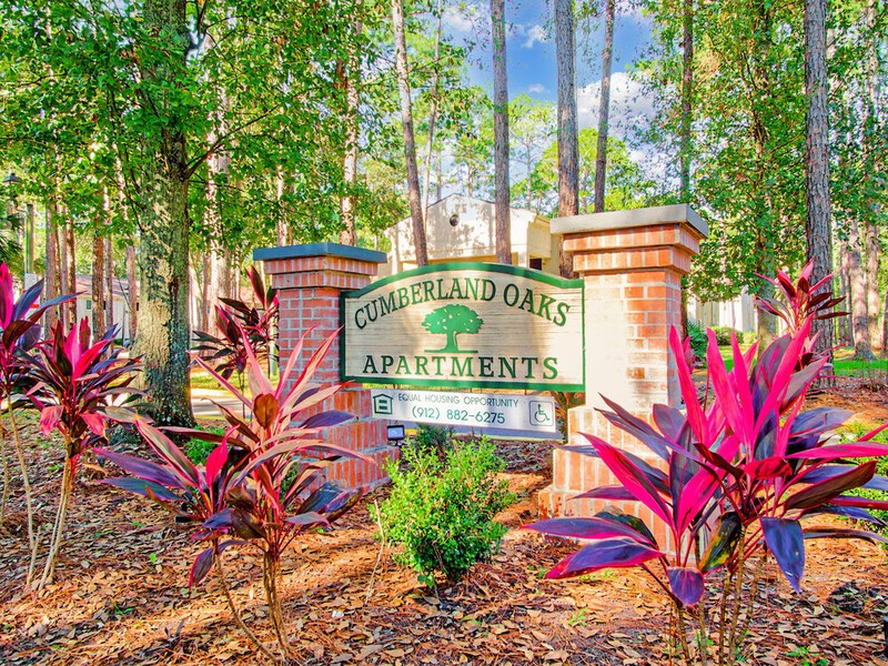 A sign for Cumberland Oaks Apartments is surrounded by plants.